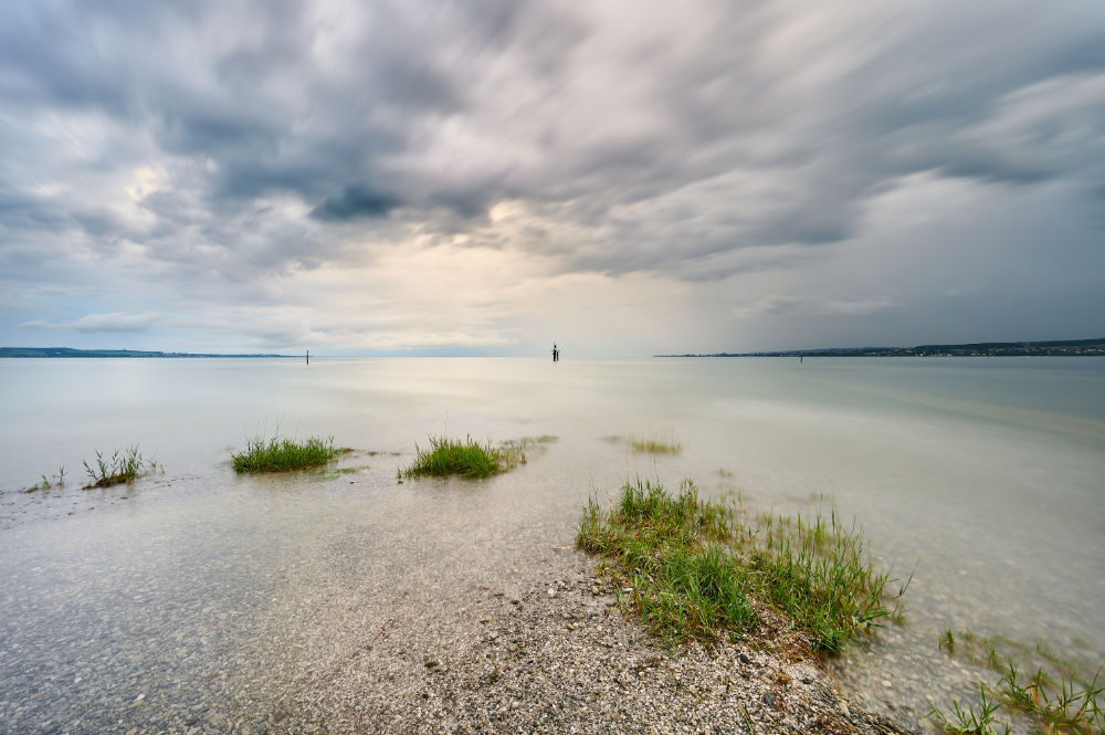 Dramatisches Wetter mit Wolken und Sonne an einem Strand am Bodensee bei Hochwasser